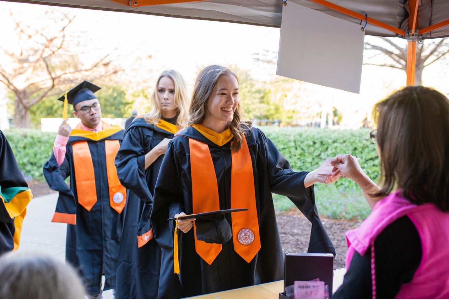 A staff member helps graduates in regalia at check in.
