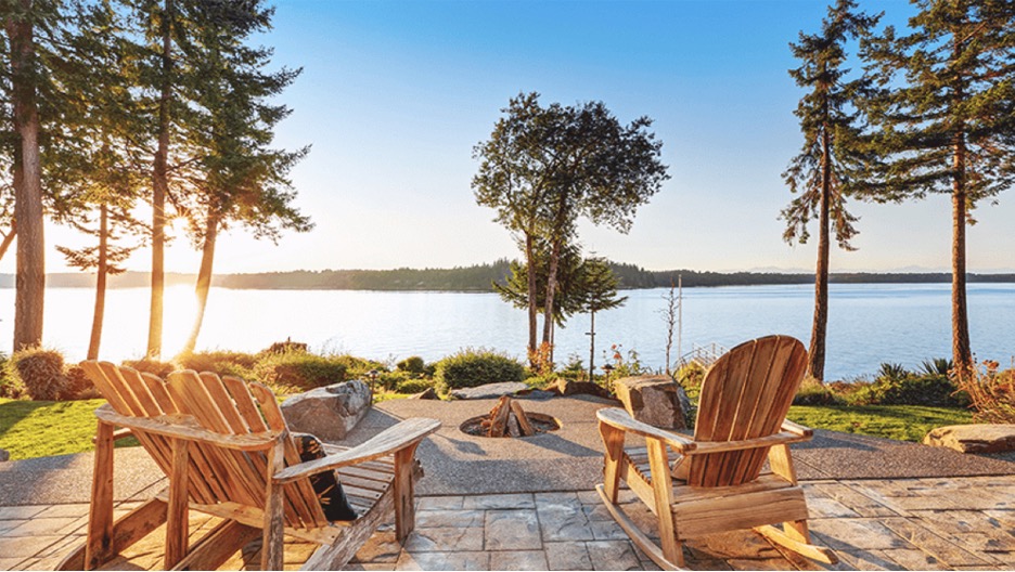 Adirondack chairs and a fire pit along the shore of a lake.