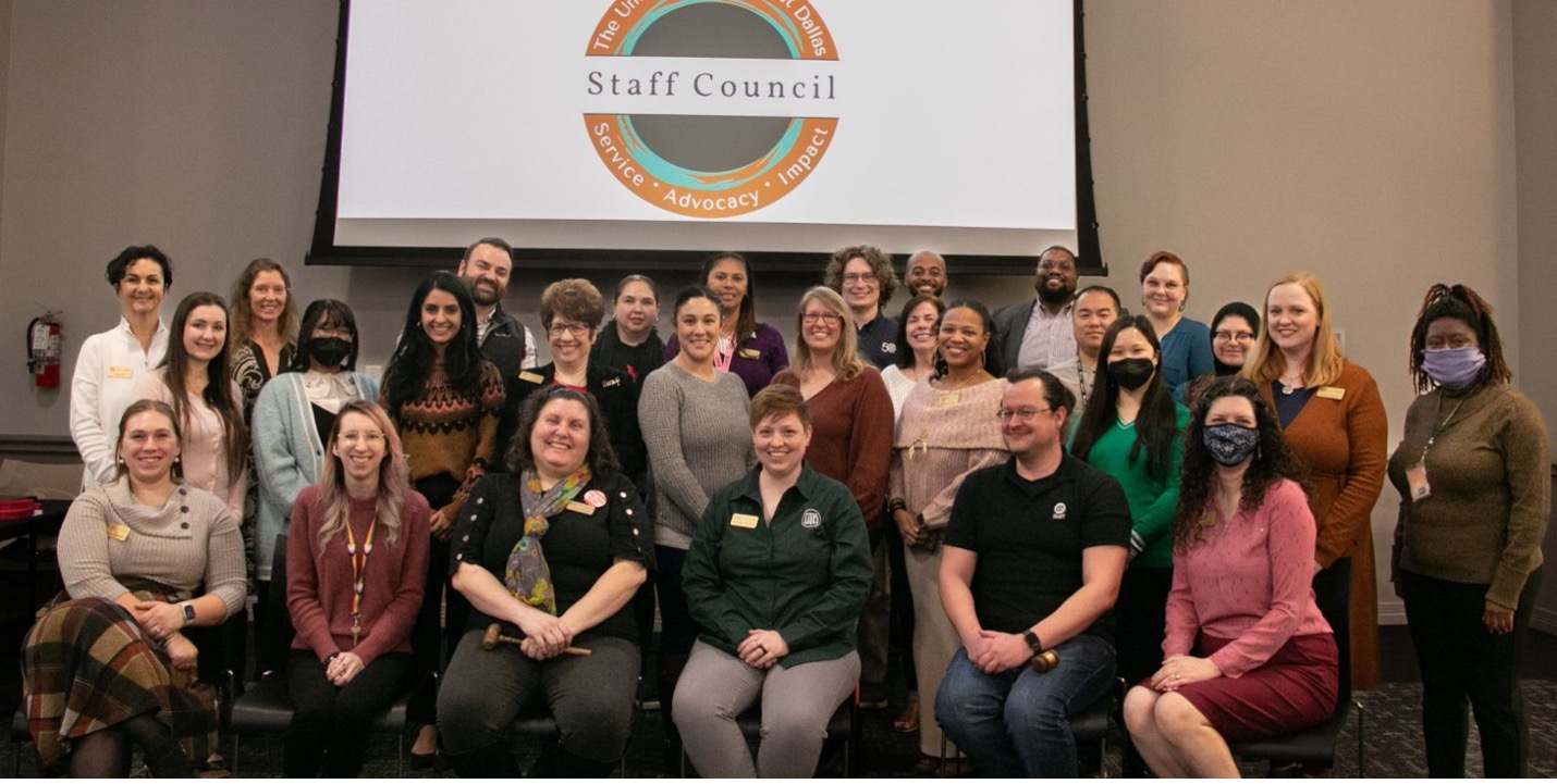 Staff Council representatives seated and standing in front of a projector screen in a room.