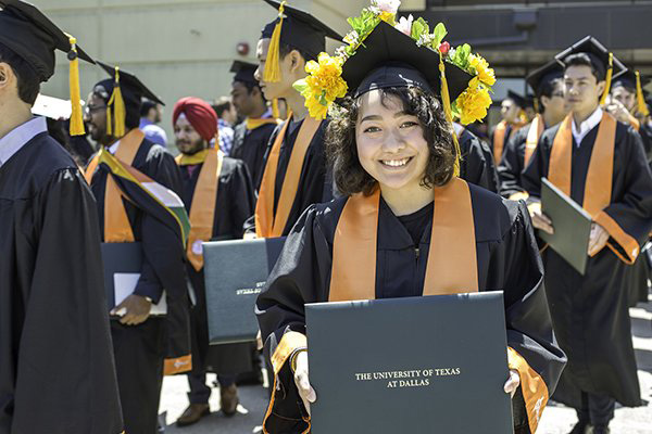 A student in graduation regalia holds a diploma holder outside of the Activity Center.