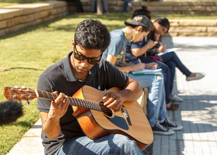 A student playing an acoustic guitar at TI Plaza