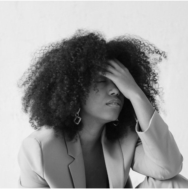 A stressed person with curly hair holding her head.